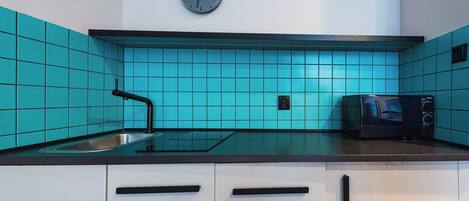 Una cocina con azulejos verde azulado, un microondas negro y un reloj en la pared.
