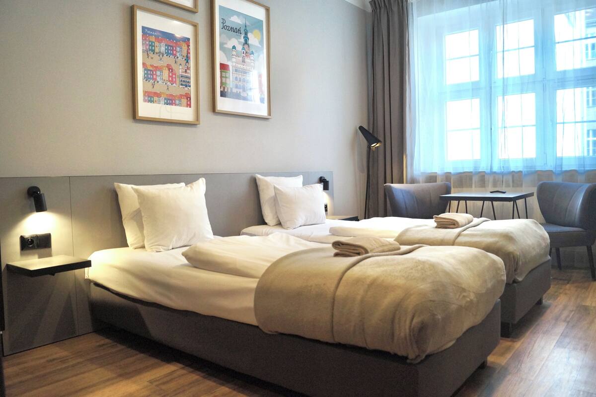 Habitación de hotel con una cama grande, dos mesitas de noche, un escritorio y una silla. Hay dos cuadros en la pared.