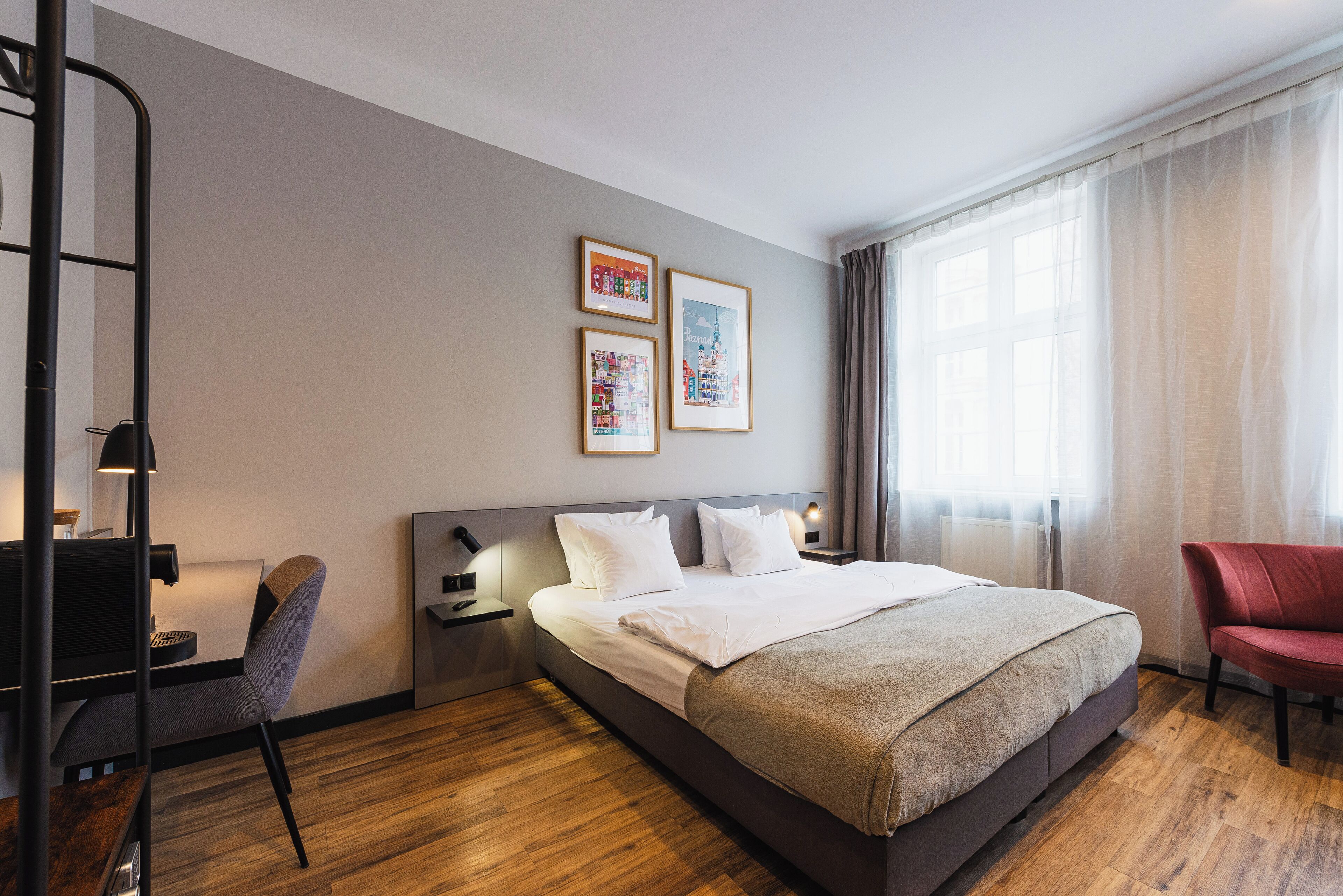 Una habitación de hotel moderna con una cama grande, un escritorio y una silla. Hay tres cuadros en la pared y una ventana con cortinas.