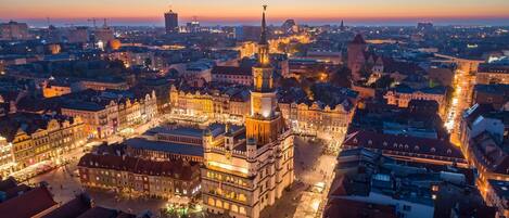 A historic city square with a prominent clock tower, surrounded by traditional buildings and a bustling street.