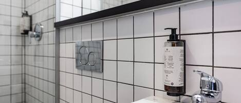 A bathroom with white tiled walls, a black countertop, a white sink, a faucet, and a soap dispenser.