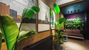 Et moderne interiør med trævæg, store grønne planter, sofa og bybillede i rammer.