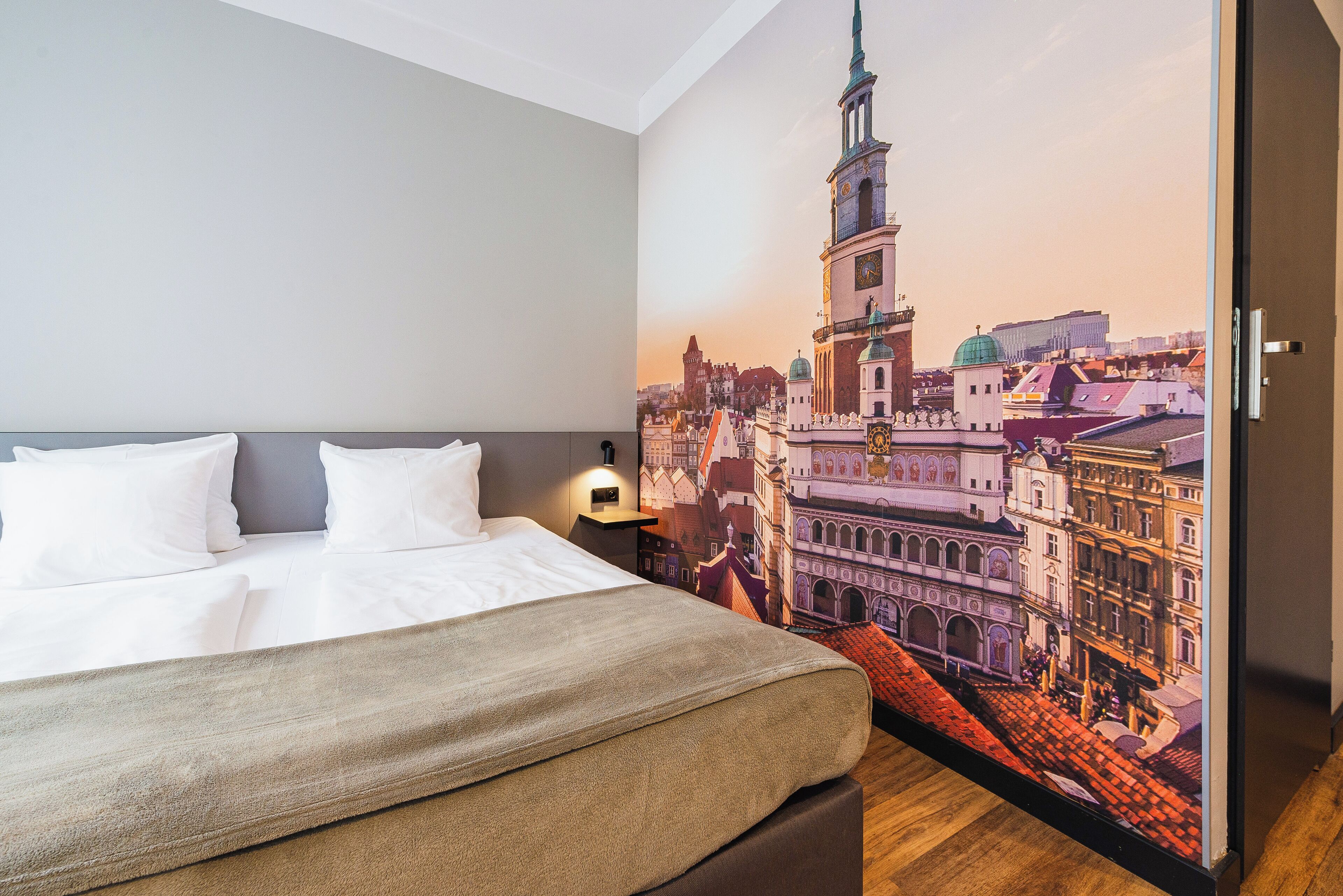 Une chambre d’hôtel avec un grand lit, une table de chevet et une fresque murale représentant un paysage urbain.
