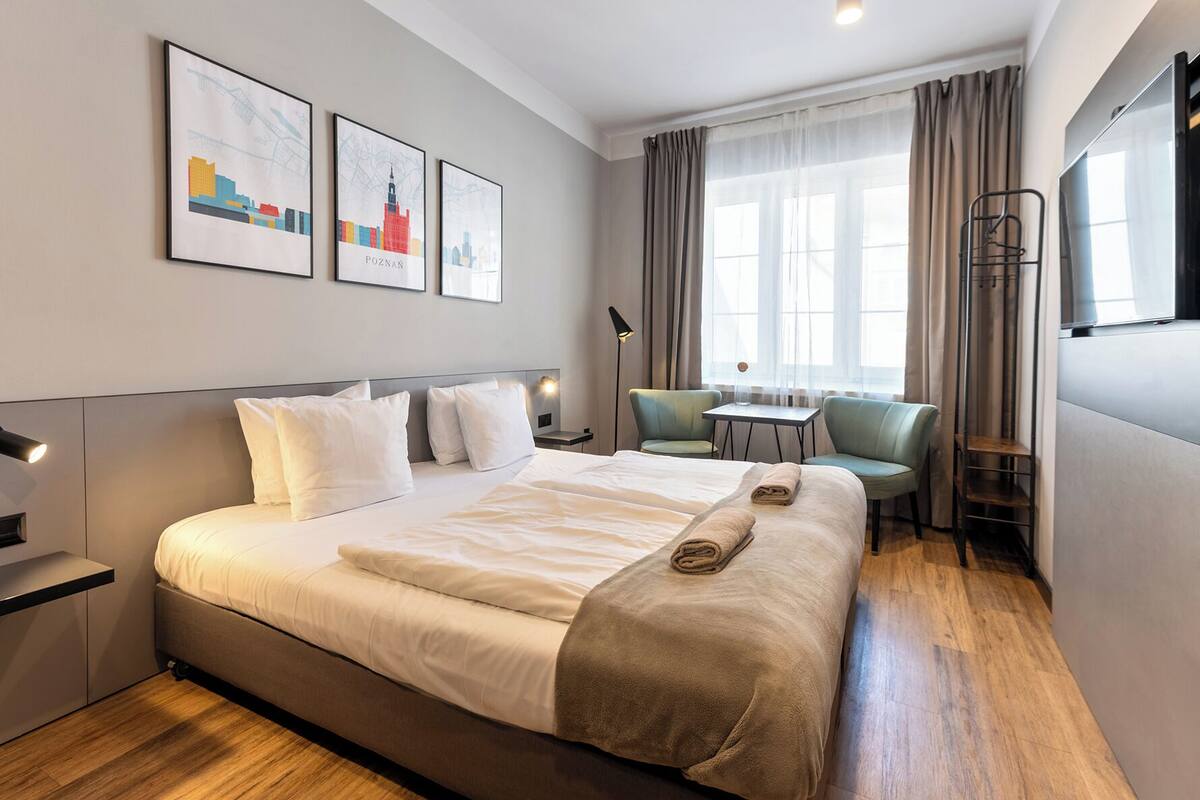 Habitación de hotel con una cama grande, un escritorio, una silla y un televisor. Hay tres cuadros en la pared.