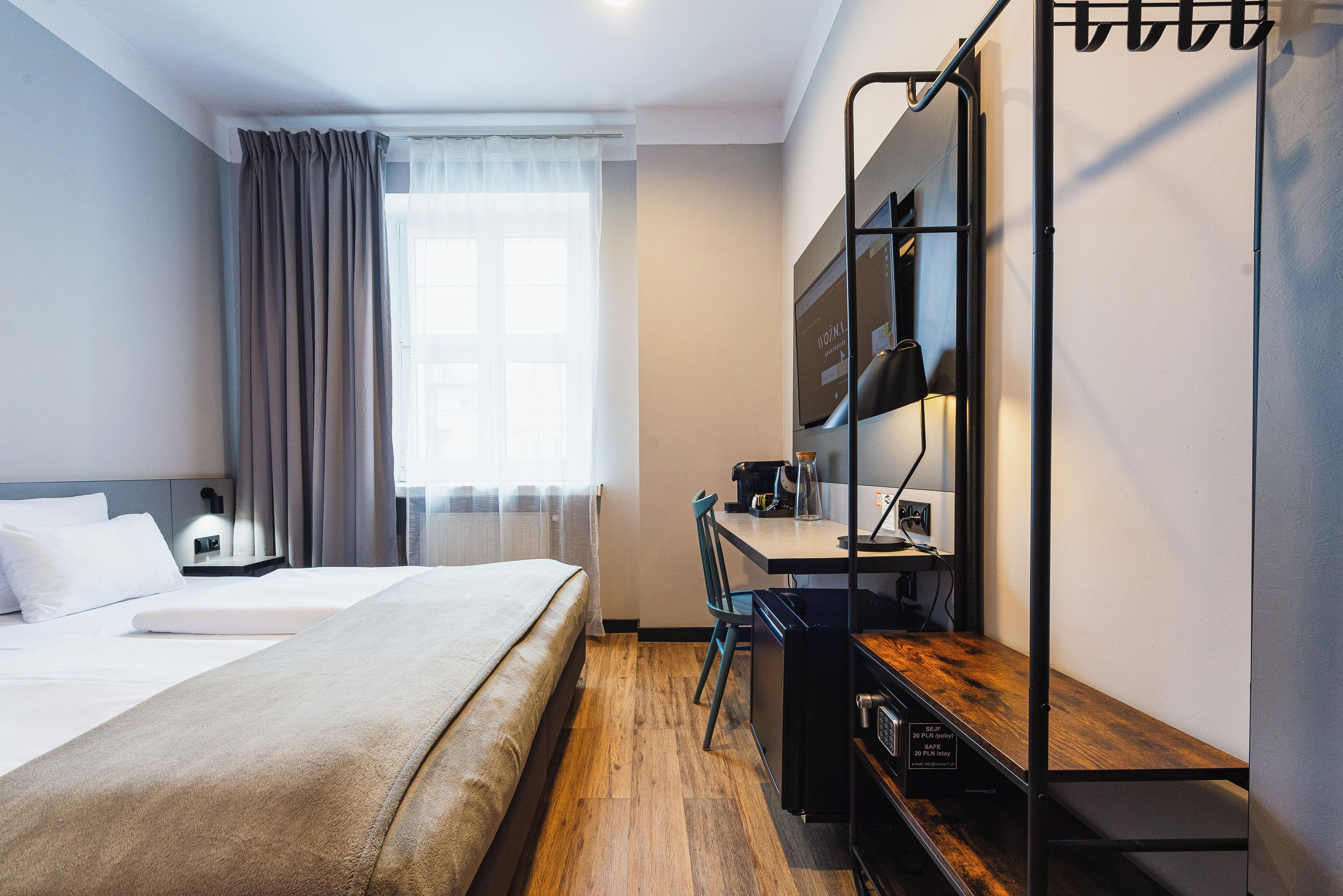 A hotel room with a bed, a desk, a chair, a small kitchenette, and a window with curtains.