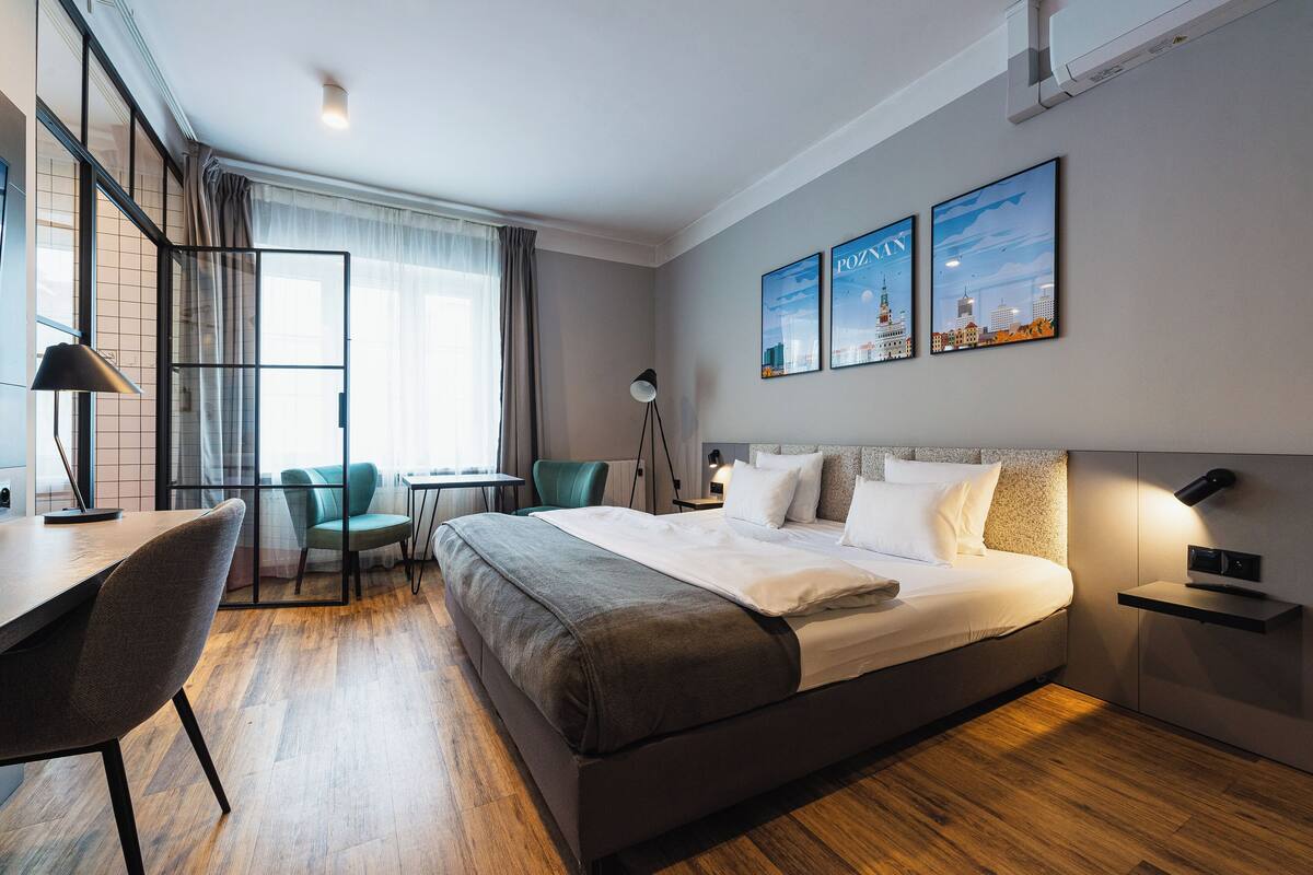 Una habitación de hotel moderna con una cama grande, un escritorio y una silla. Hay dos cuadros en la pared y una lámpara en la mesita de noche.
