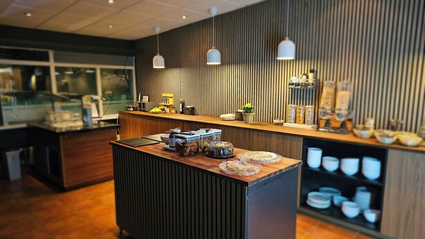 A modern reception area with a wooden reception desk, pendant lighting, and a wall-mounted display with various items. - Hotel Austur (Fjardabyggd)