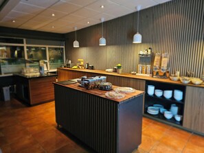 Uma área de recepção moderna com balcão de madeira, iluminação pendente e um painel de parede com diversos objetos.
