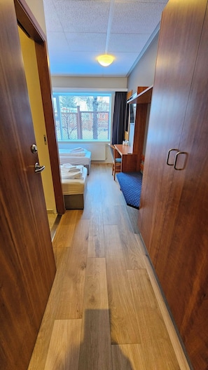 En smal hall med trägolv, en säng, ett skrivbord och en garderob.