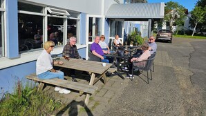 A group of people seated at an outdoor table with a view of a building with large windows and a covered patio area. - Hotel Austur (Fjardabyggd)