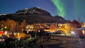 A town with a mountain in the background and the Northern Lights in the sky. - Hotel Austur (Fjardabyggd)