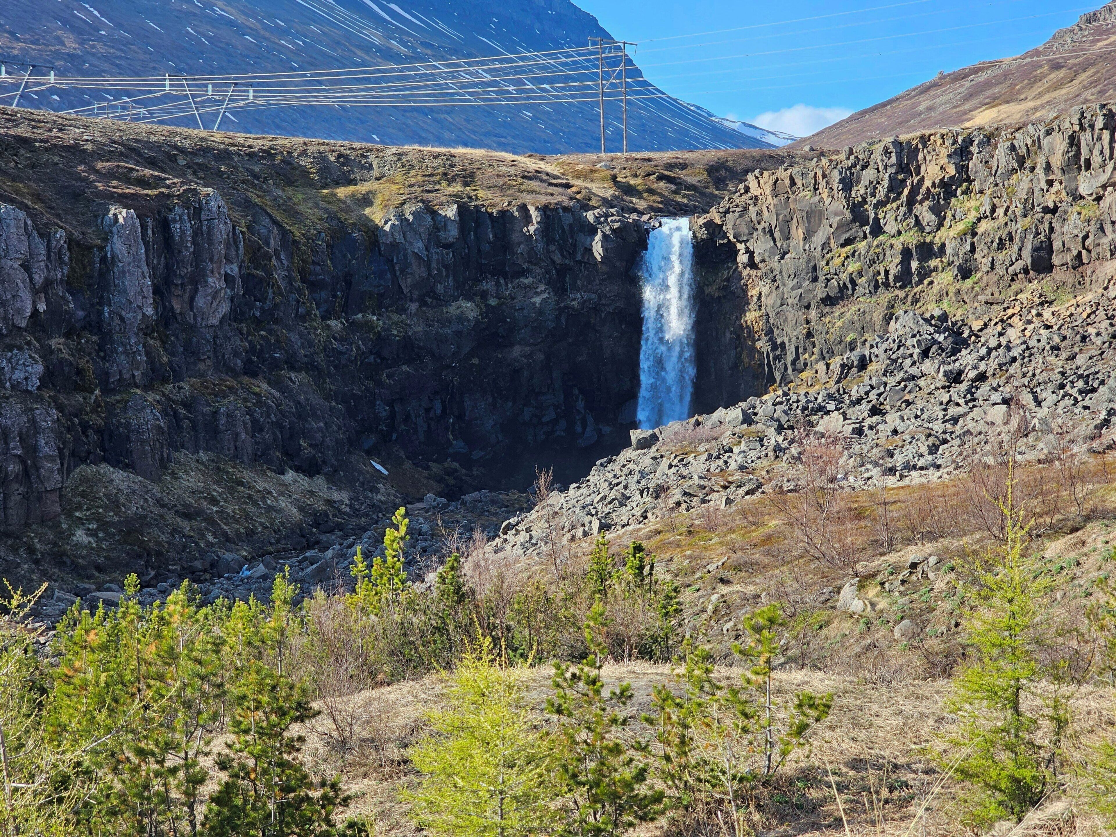 A mountainous landscape with a waterfall, rocky terrain, and sparse vegetation.