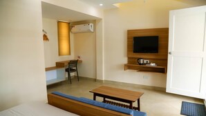Habitación de hotel compacta con cama, un banco de madera, una mesita pequeña, un televisor montado en la pared y un área de escritorio con silla.