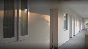 Un pasillo largo y estrecho con una serie de puertas a un lado y ventanas al otro.
