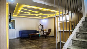 Una sala de estar moderna con un sofá azul, una mesa de centro y una mesita con una cafetera. Se ve una escalera con barandilla que sube a otro nivel.
