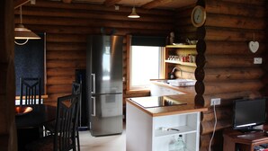 A log cabin interior with a kitchen area, including a refrigerator, dining table, chairs, and a small island with a sink. - Akureyri Log Cabin (Akureyri)