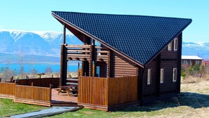 A wooden cabin with a sloped roof, a deck, and a view of mountains and a lake. - Akureyri Log Cabin (Akureyri)