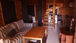 A log cabin interior with a sofa, wooden table, and a spiral staircase. - Akureyri Log Cabin (Akureyri)
