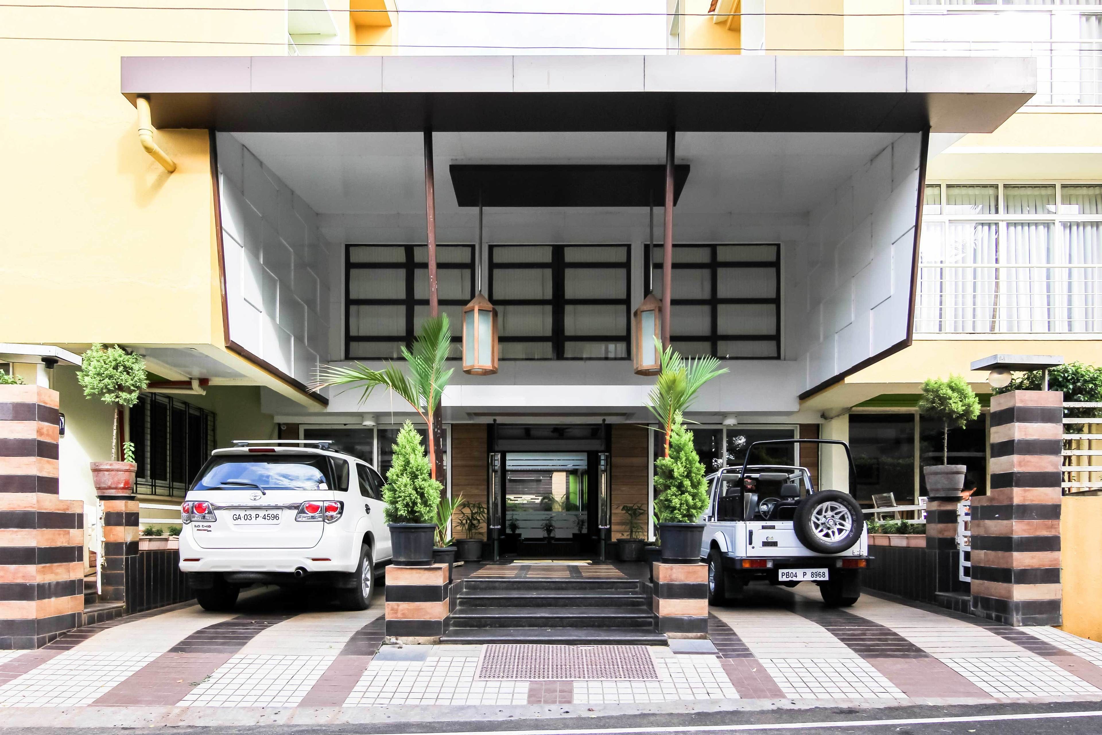 A building entrance with two cars parked on either side, a set of stairs leading up to the entrance, and potted plants on either side.