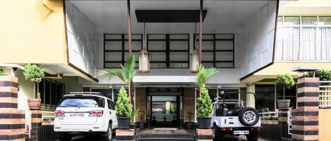 A building entrance with two cars parked on either side, a set of stairs leading up to the entrance, and potted plants on either side.