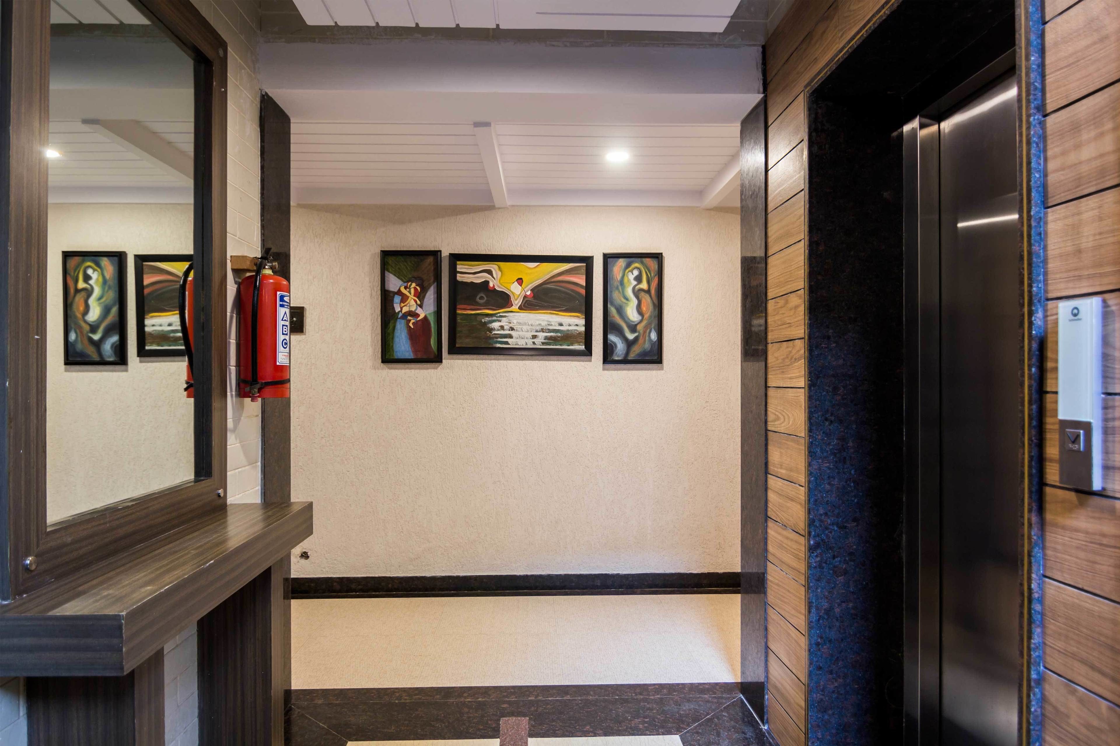 Een gang met kunstwerken aan de muur, een brandblusser en een lift.