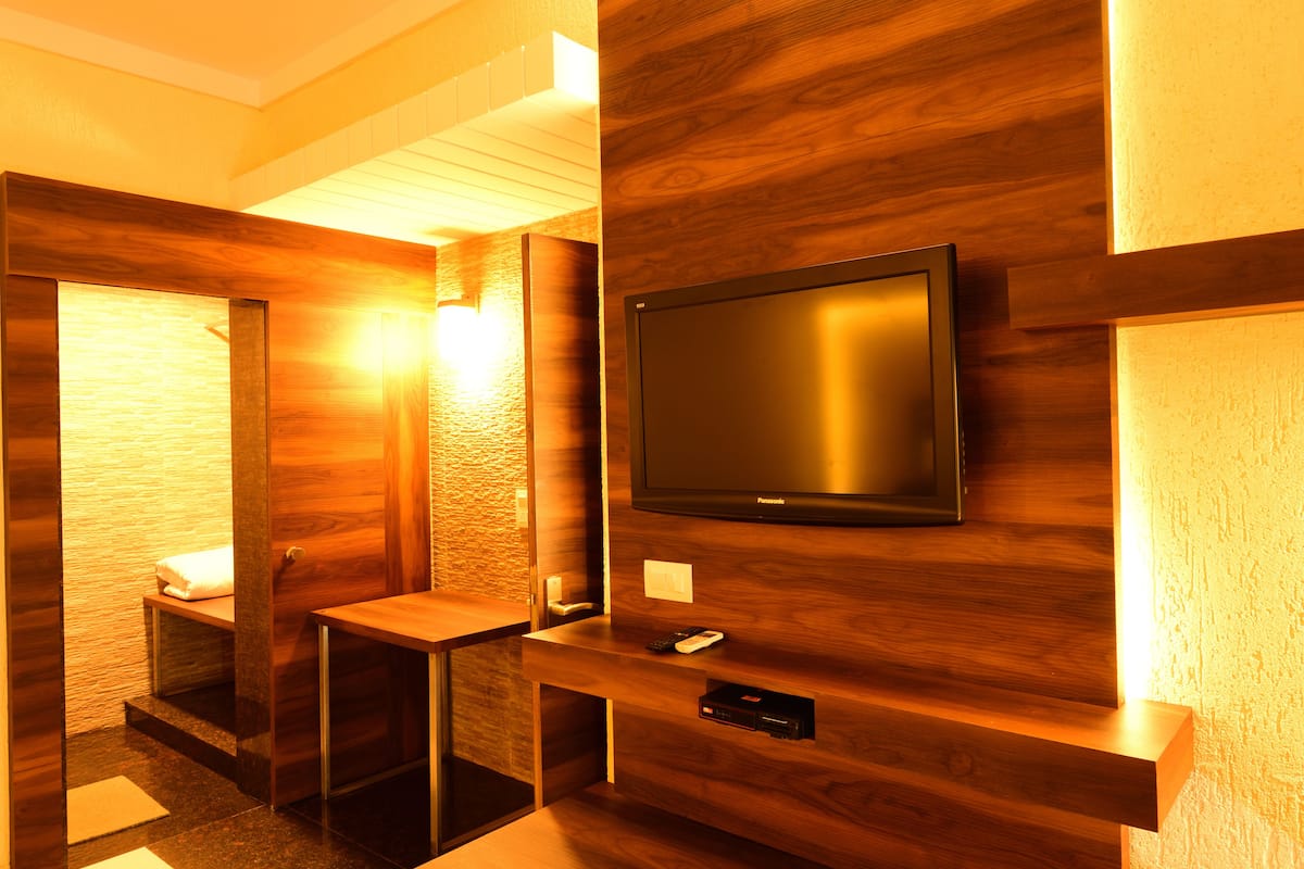 Une salle de bain moderne avec un meuble-lavabo en bois, des toilettes et un téléviseur fixé au mur.