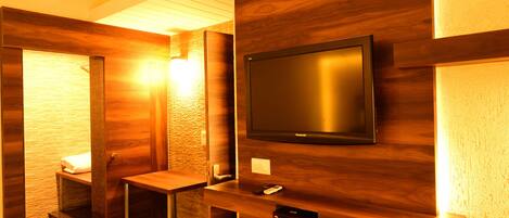 A modern bathroom with a wooden vanity, a toilet, and a mounted television.