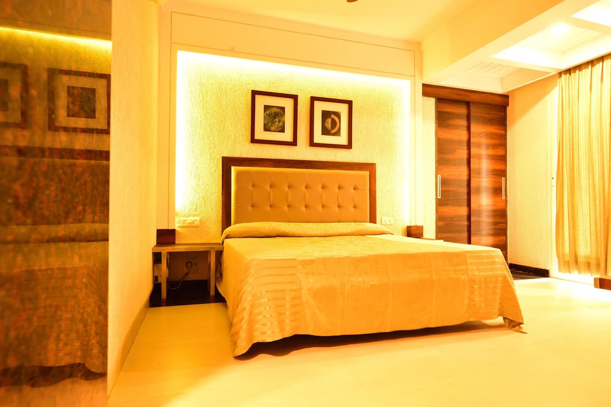 Une chambre d’hôtel avec un grand lit, une table de chevet, une lampe fixée au mur et une porte avec un panneau en bois.