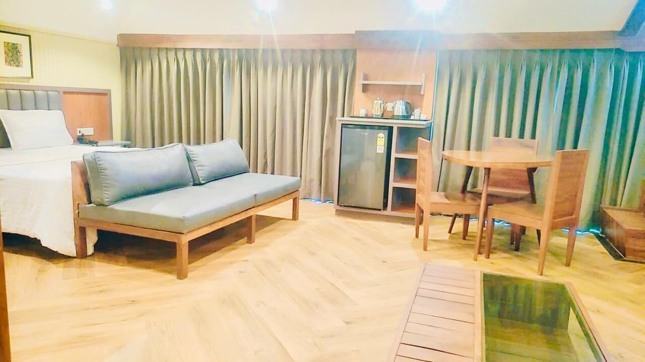 Een hotelkamer met een bed, een slaapbank, een eettafel met stoelen, een kleine kitchenette en een groot raam met gordijnen.
