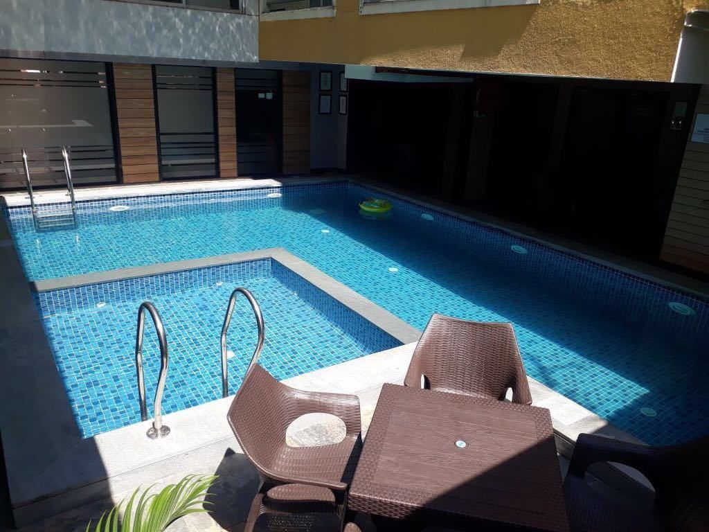 Una piscina con dos escaleras de metal, rodeada de sillas de mimbre marrón y una mesa.