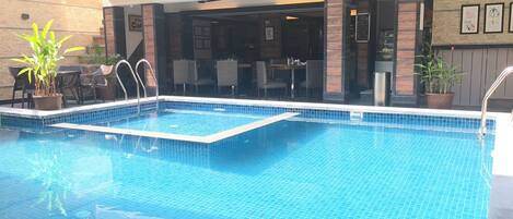 Piscina rectangular con borde de azulejos, rodeada de mobiliario exterior y plantas en macetas.