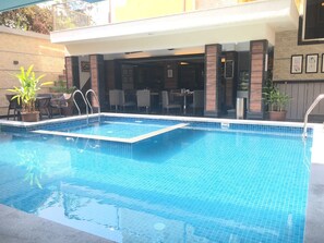 Piscina rectangular con borde de azulejos, rodeada de mobiliario exterior y plantas en macetas.