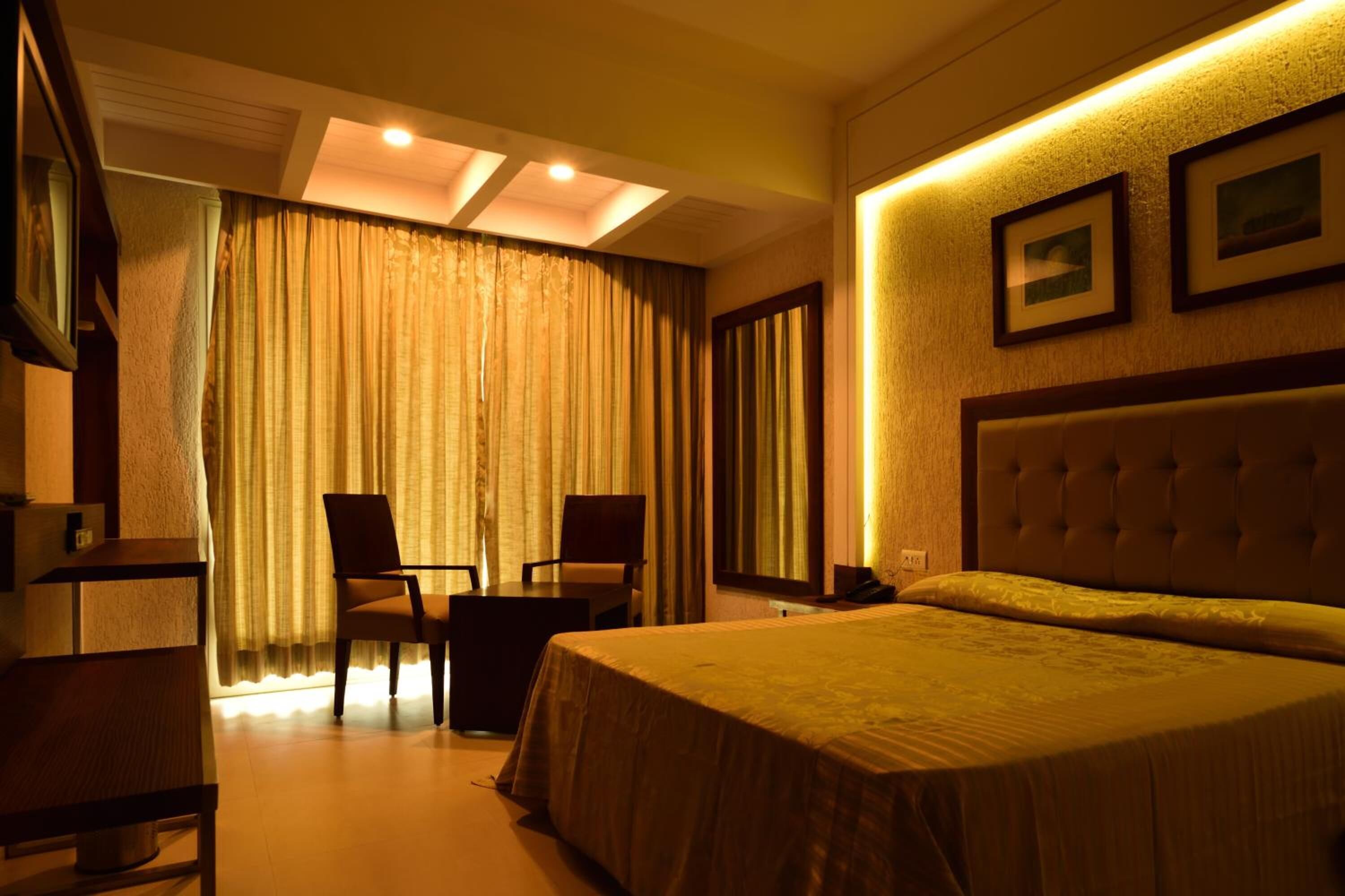 Habitación de hotel con cama, dos sillas, escritorio y un ventanal con cortinas.
