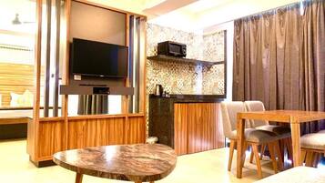 A modern living room with a flat-screen TV, a wooden dining table, and a kitchen area with a microwave.