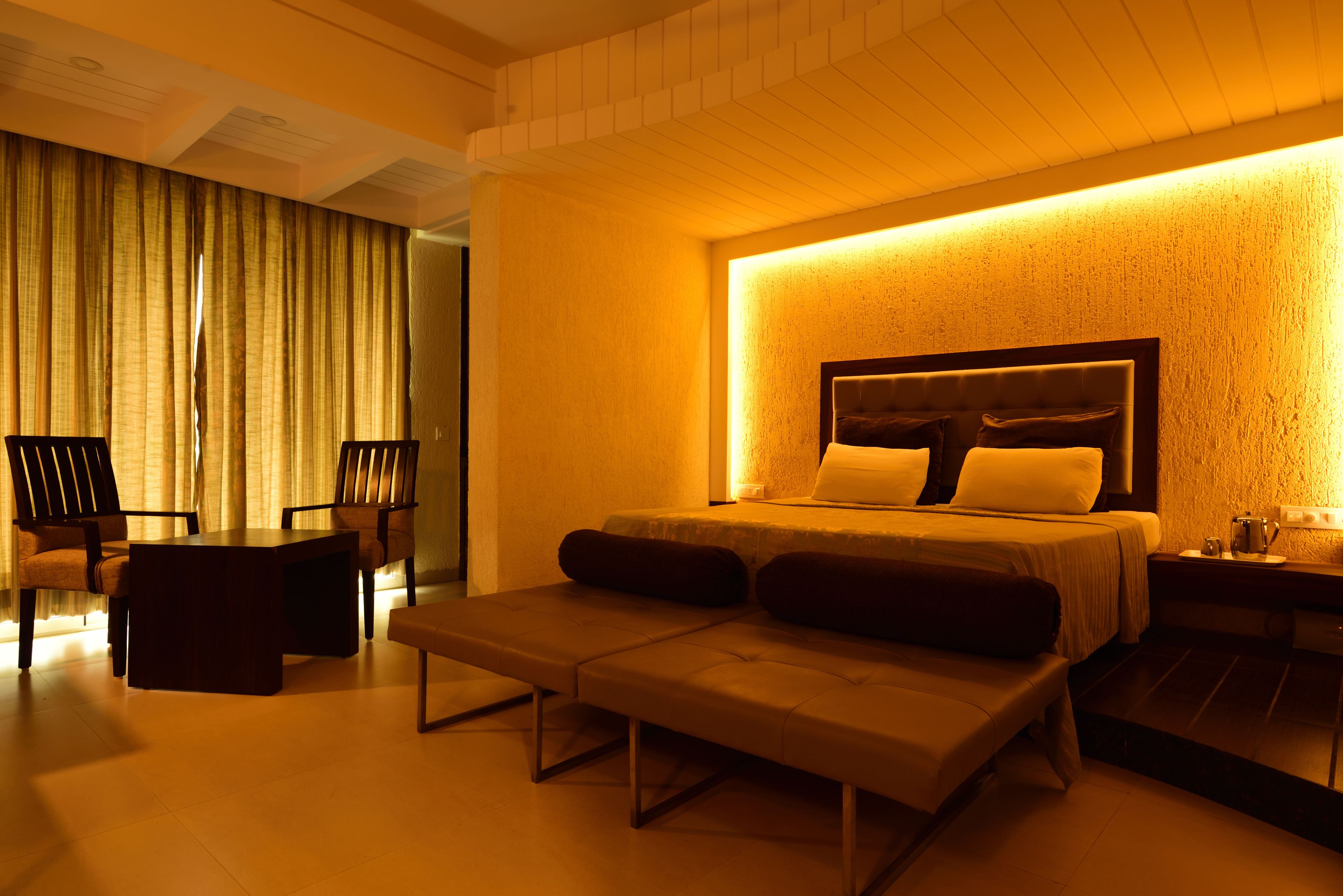 Une chambre d’hôtel comprenant un lit, une banquette, deux chaises, une table et une table de chevet.