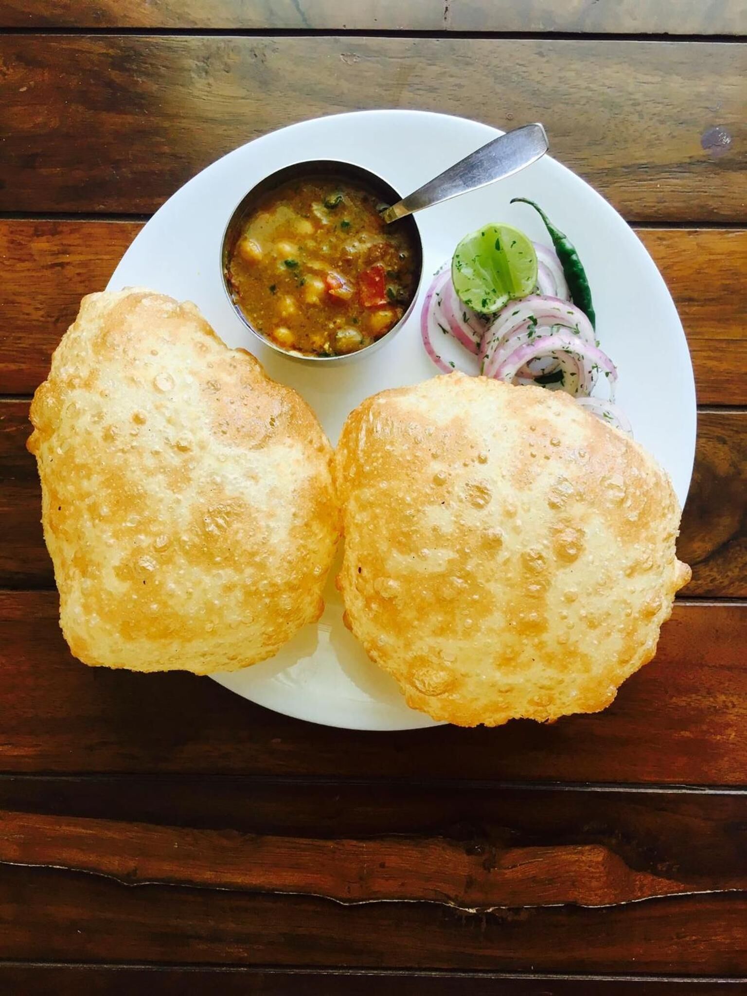 A plate with two fried breads, a bowl of soup, and sliced onions and a green chili.