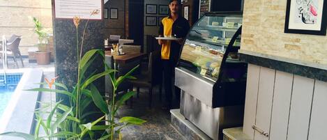 Un restaurante con zona de piscina, un cartel de menú y una barra con alimentos.