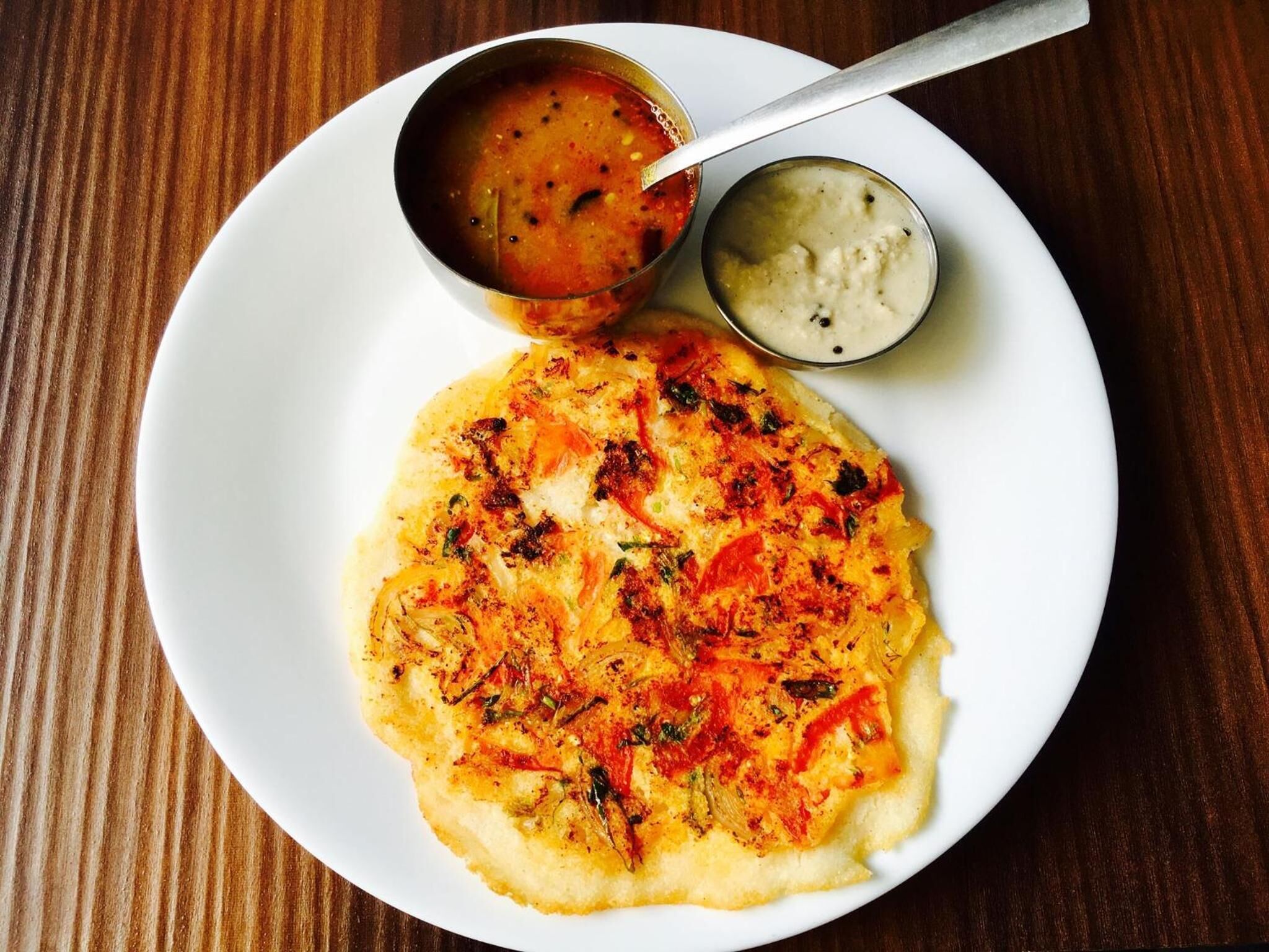 Un plato con un pan plano cubierto de vegetales y un recipiente pequeño con salsa.