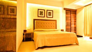 A hotel room with a large bed, a headboard, two framed pictures on the wall, and a wooden wardrobe.