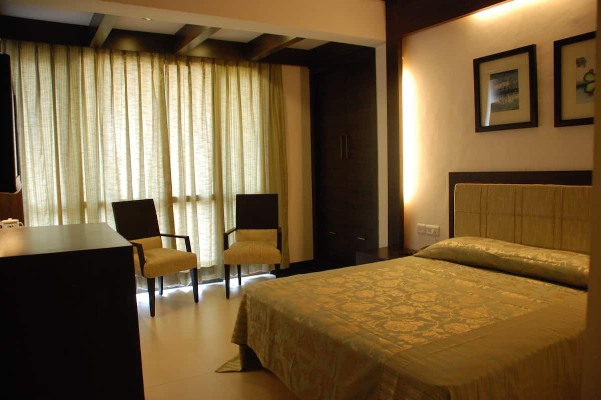 Une chambre d’hôtel avec un lit, deux chaises, un bureau et une grande fenêtre avec des rideaux.