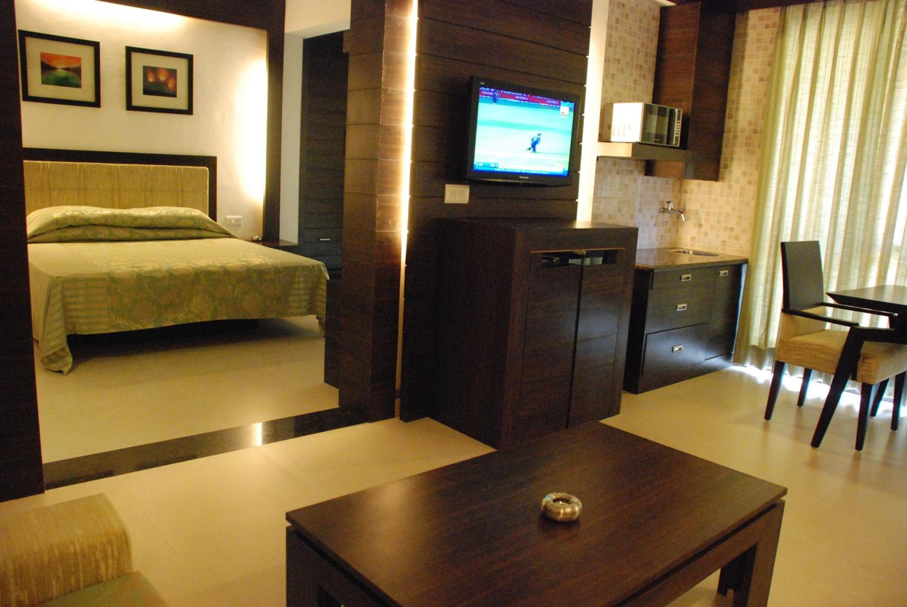 Una habitación de hotel con cama, televisor montado en la pared, escritorio pequeño y una silla.