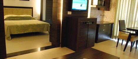 Una habitación de hotel con cama, televisor montado en la pared, escritorio pequeño y una silla.