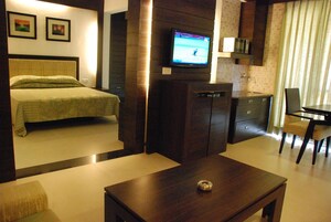 Una habitación de hotel con cama, televisor montado en la pared, escritorio pequeño y una silla.