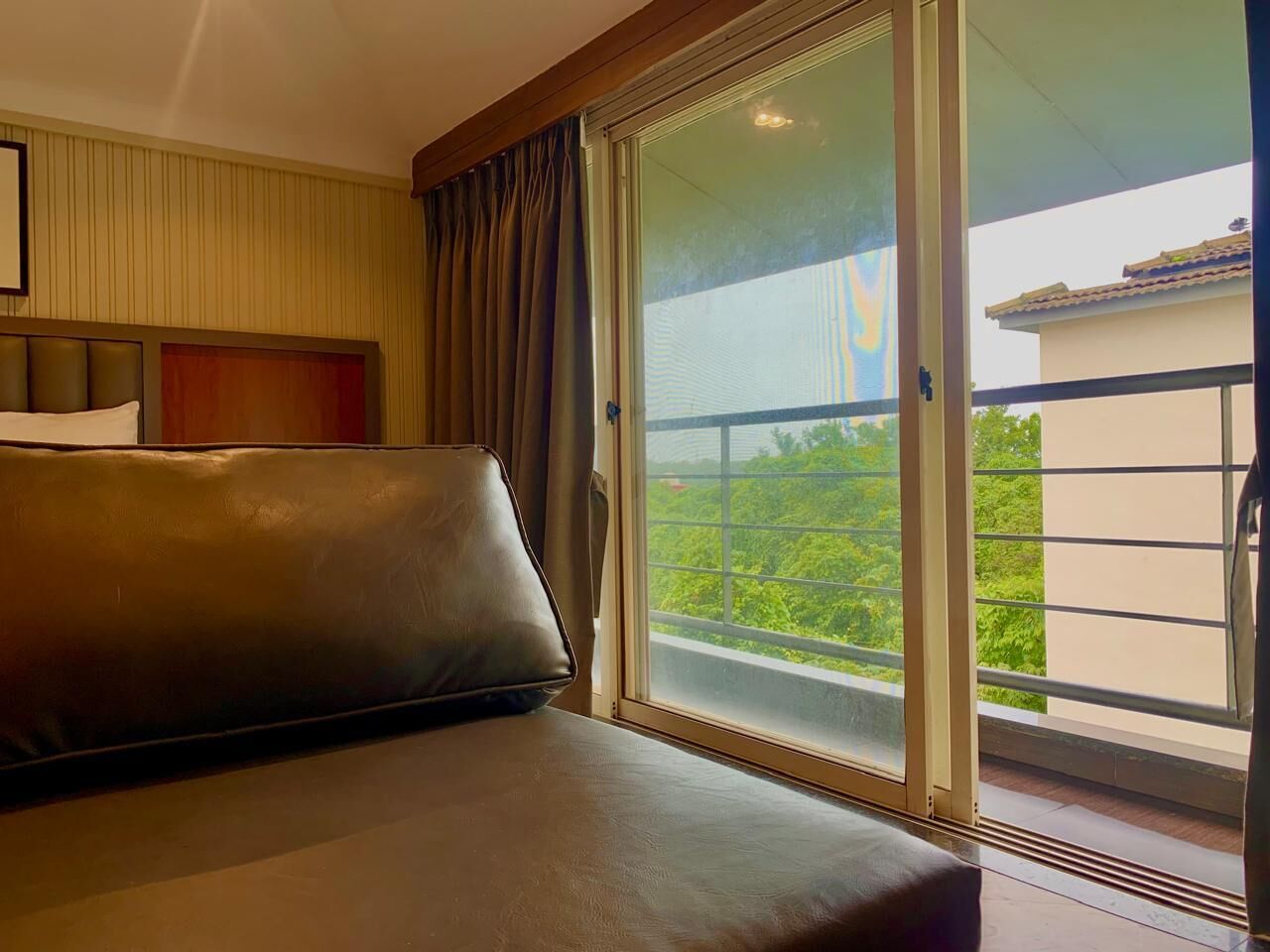 Habitación de hotel con un amplio ventanal corredera que da a un balcón con vistas a zonas verdes.