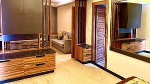 A modern living room with a sofa, coffee table, and wooden cabinets. There is a door leading to another room and a large mirror on the wall. - Le Magnifique (Alto de Porvorim)