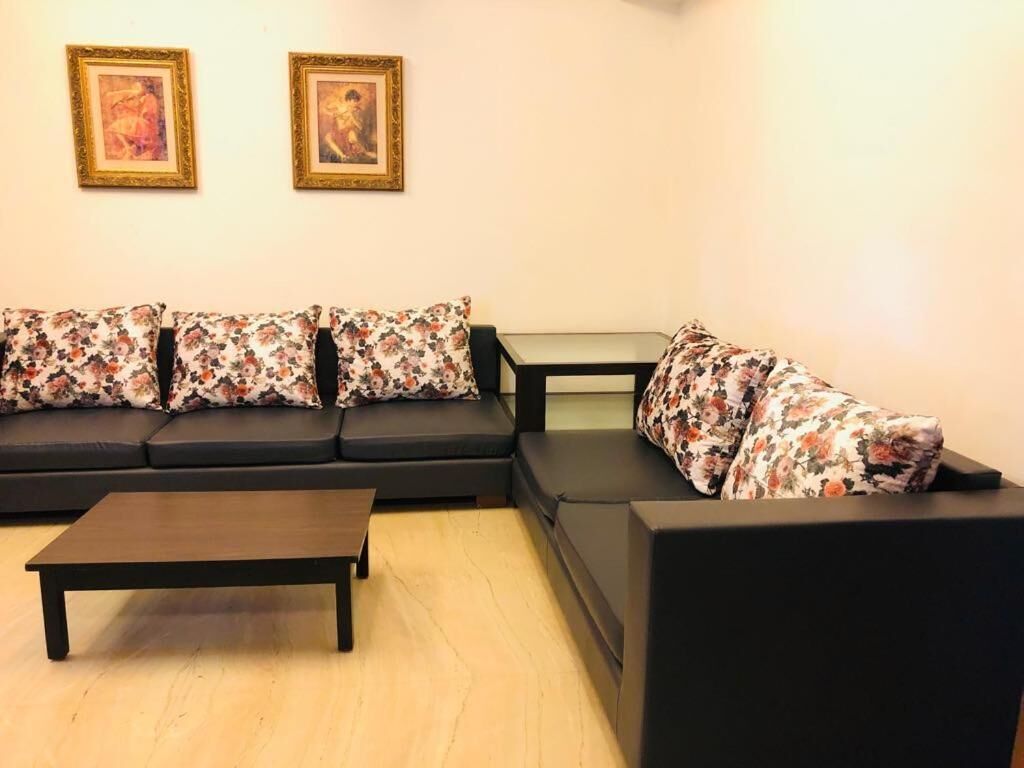A living room with a black sofa, a matching armchair, a small coffee table, and two framed pictures on the wall.