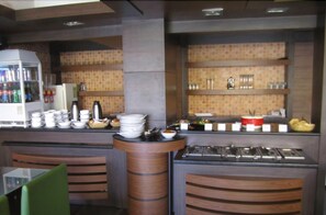 Montaje tipo bufé con múltiples estaciones de servicio, un refrigerador con bebidas y una variedad de platos exhibidos en estantes.