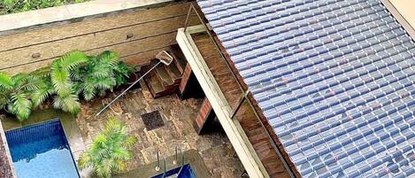Una piscina en la azotea con suelo de baldosas azules, rodeada de exuberante vegetación y una zona con plataforma de madera.