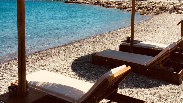 Een strand met rieten parasols en houten ligstoelen.