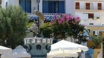 A building with a sign reading "STUDIOS & ROOMS MAISTRALI" and a fountain with a statue in front.
